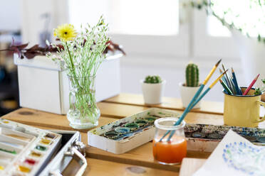 Aquarellfarben mit Blumenvase und Pinseln auf Holztisch zu Hause - AFVF06493