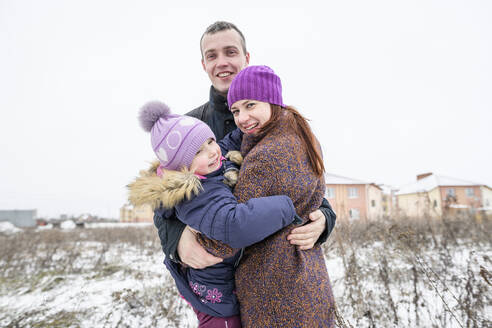 Glückliche Familie umarmt auf schneebedeckten Feld gegen klaren Himmel - EYAF01104