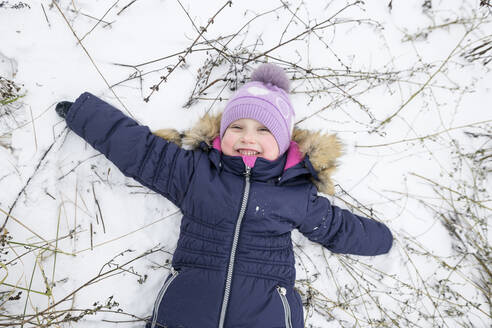 Glückliches Mädchen liegt mit ausgestreckten Armen im Schnee - EYAF01105