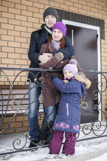 Nettes Mädchen mit Eltern vor dem Haus im Winter stehend - EYAF01106
