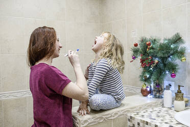 Glückliche Frau, die ihrer Tochter beim Zähneputzen zu Hause hilft - EYAF01110