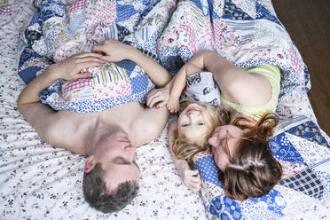 Happy girl lying with parents in bed at home - EYAF01113