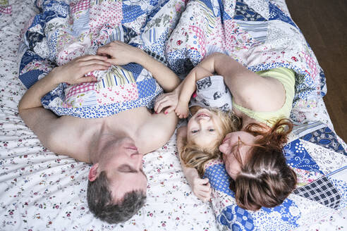 Glückliches Mädchen mit Eltern zu Hause im Bett liegend - EYAF01113