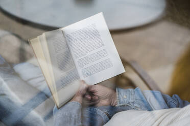 Ausgeschnittenes Bild eines älteren Mannes, der ein Buch liest und sich auf dem Sofa ausruht, gesehen durch ein Glasfenster - AFVF06568