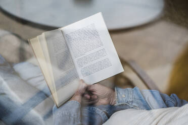 Cropped image of senior man reading book while relaxing on sofa seen through glass window - AFVF06568