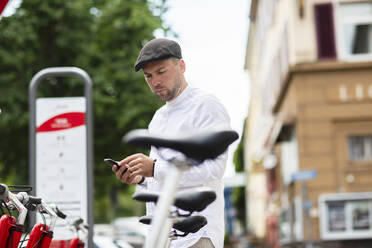 Man renting bicycle through smart phone at parking station - SGF02657