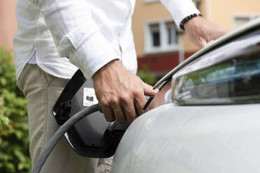 Mann lädt Elektroauto an der Tankstelle - SGF02660