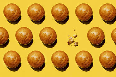 Pattern of rows of muffins against yellow background with single one missing - GEMF03809