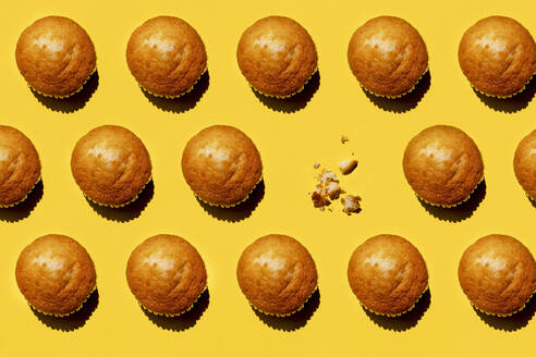 Muster aus Reihen von Muffins vor gelbem Hintergrund, wobei ein einzelner Muffin fehlt - GEMF03809