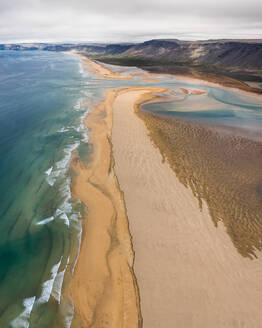 Luftaufnahme von Raudisandur, einem der wenigen gelben Strände in Island. Ein Delta eines kleinen Flusses erzeugt abstrakte Muster im weißen Sand. Westfjorde, Island. - AAEF08769