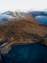 Luftaufnahme der schneebedeckten Gipfel des Thyrill-Gebirges und der kurvenreichen Straße um den Hvalfjordur-Fjord in Westisland, im Hintergrund ist der Berg Hvalfell zu sehen. - AAEF08771