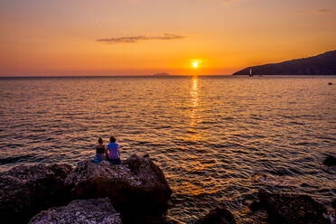 Aerial view of a couple watching the shore of the bay at sunset in Komiza, Croatia - AAEF08806