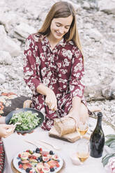 Lächelnde junge Frau schneidet Brot auf dem Tisch und genießt es mit einem Freund beim Picknick - ALBF01244