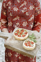 Close-up of young woman holding savory pie on serving board while standing outdoors - ALBF01251