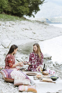 Frau bietet ihrer Freundin beim Picknick am Seeufer Obstsalat an - ALBF01255