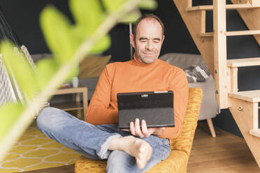 Älterer Geschäftsmann, der bei der Arbeit zu Hause ein digitales Tablet benutzt - UUF20439
