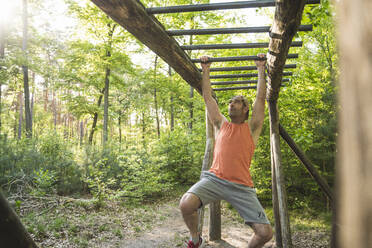 Mature man hanging from monkey bars while exercising at park - UUF20470