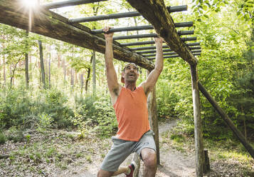 Happy man hanging from monkey bars while exercising at park - UUF20471