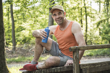 Happy mature man sitting with water bottle at park - UUF20473