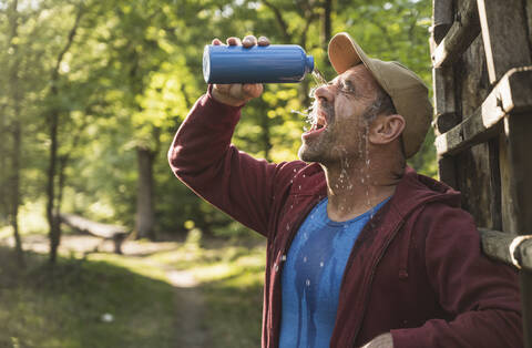 Älterer Mann gießt sich im Park Wasser aus einer Flasche ins Gesicht, lizenzfreies Stockfoto
