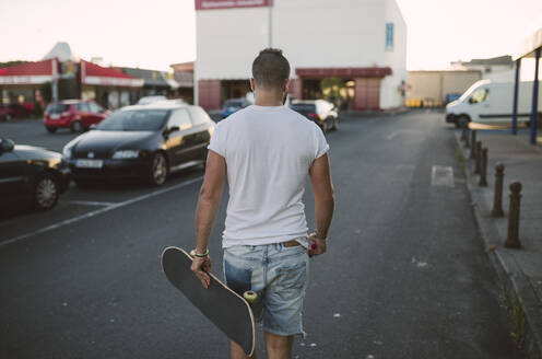 Junger Mann mit Skateboard auf der Straße in der Stadt - RAEF02382