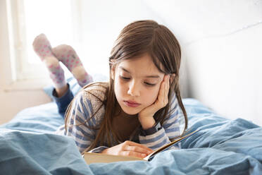 Porträt eines kleinen Mädchens, das auf dem Bett liegt und ein Buch liest - LVF08924