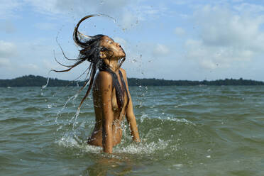 Oben ohne sinnliche junge Frau, die sich die Haare wirft, während sie im Meer gegen den Himmel steht - EAF00020