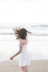 Junge Frau in weißem Kleid steht am Strand gegen den klaren Himmel - FVSF00375