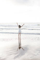 Young woman with arms raised standing at shore against sky - FVSF00377