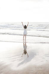 Carefree young woman with arms raised standing at shore against clear sky - FVSF00378