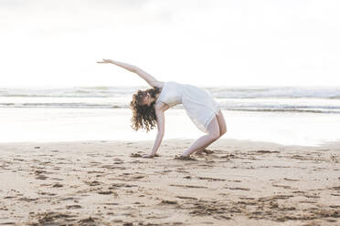 Junge Frau im weißen Kleid tanzt am Strand gegen den klaren Himmel - FVSF00381