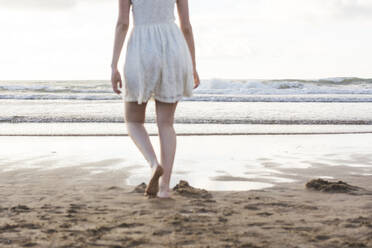 Junge Frau in weißem Kleid läuft barfuß am Strand gegen den klaren Himmel - FVSF00385