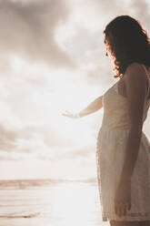 Young woman wearing white dress standing against sea during sunset - FVSF00391