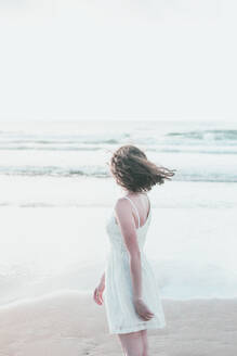 Junge Frau in weißem Kleid schaut auf das Meer gegen den klaren Himmel - FVSF00401