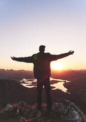 Young male tourist standing with arms outstretched on mountain during sunset, Leon, Spain - FVSF00413