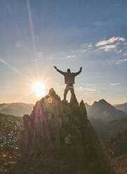Silhouette eines männlichen Wanderers, der mit ausgestreckten Armen auf einem Berg bei Sonnenuntergang steht, Leon, Spanien - FVSF00423