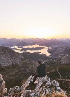 Männlicher Wanderer auf einer Klippe sitzend bei Sonnenuntergang und klarem Himmel, Leon, Spanien - FVSF00429