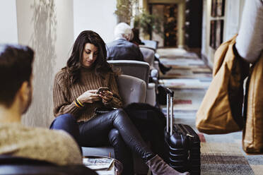 Mittlere erwachsene Frau, die ein Mobiltelefon benutzt, während sie vor ihrem Freund im Hotel sitzt - MASF18384