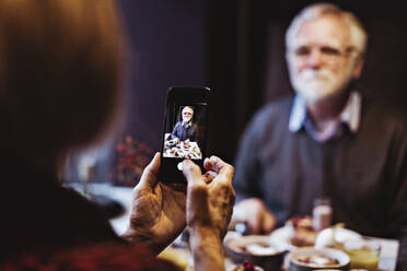 Ältere Frau fotografiert Mann durch Smartphone beim Frühstück am Tisch im Hotel - MASF18400