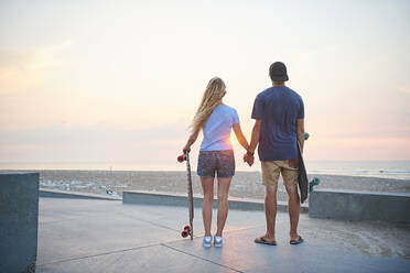 Ein junges Paar, Mann und Frau, fährt bei Sonnenuntergang am Strand Skateboard. - ISF24175