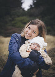 A woman with an infant is standing on the Californian beach - CAVF84508