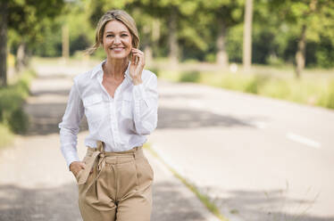 Confident mature businesswoman smiling while standing on road - UUF20507