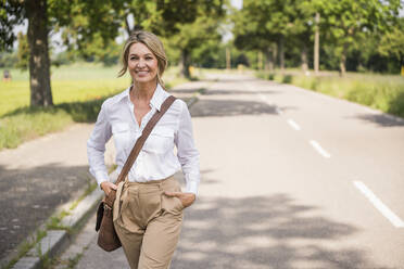 Confident businesswoman carrying shoulder bag while walking on road - UUF20510
