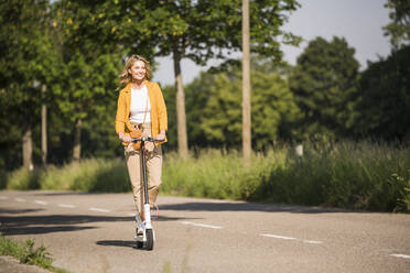 Ältere Frau fährt elektrischen Roller auf der Straße an einem sonnigen Tag - UUF20521