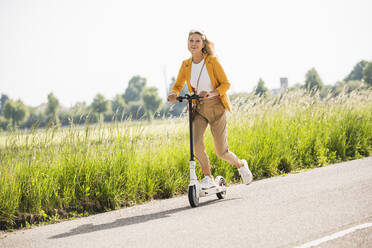 Playful reife Frau Reiten elektrische Push-Roller auf der Straße im Sommer - UUF20529
