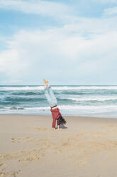 Young woman doing handstand at Ursa beach against sky, Portugal - FVSF00434