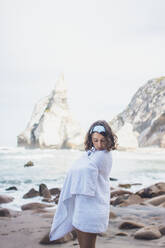 Junge Frau, eingewickelt in ein Handtuch, am Strand von Ursa, Portugal - FVSF00438