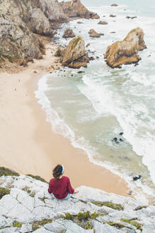 Junge Frau schaut auf das Meer, während sie auf einem Berg sitzt, Strand Ursa, Portugal - FVSF00442