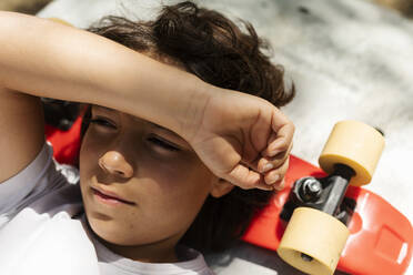 Nahaufnahme eines nachdenklichen Jungen, der auf einem Skateboard liegend wegschaut - VABF02978