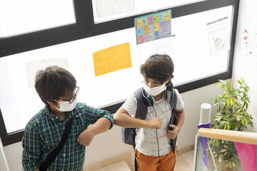 Maskierte Schüler stoßen sich mit dem Ellbogen an, während sie auf einer Treppe stehen - VABF02982